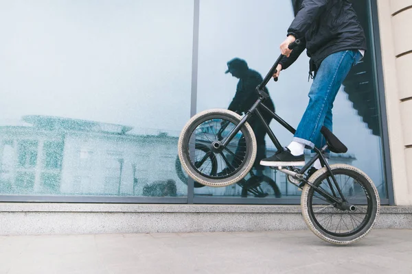 Een man rijdt een fiets op het achterwiel van een Bmx tegen een etalage van glas. Een tiener maakt trucs op een Bmx fiets. BMX concept. — Stockfoto