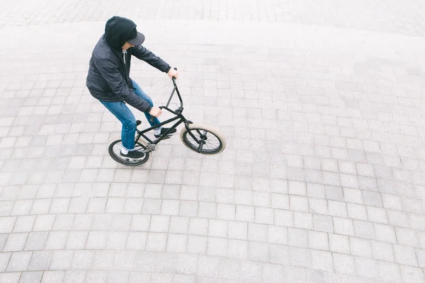 A young man in casual clothing, riding a bike on the rear wheel of a BMX. The minimalist photo of the BMX cyclist is from above. bmx culture — Stock Photo, Image