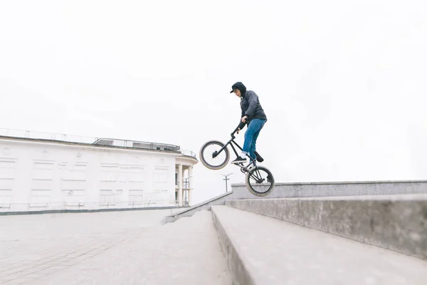 Un giovane salta su una bici BMX lungo le scale. Bmx freestyle sullo sfondo del paesaggio urbano. concept BMX . — Foto Stock