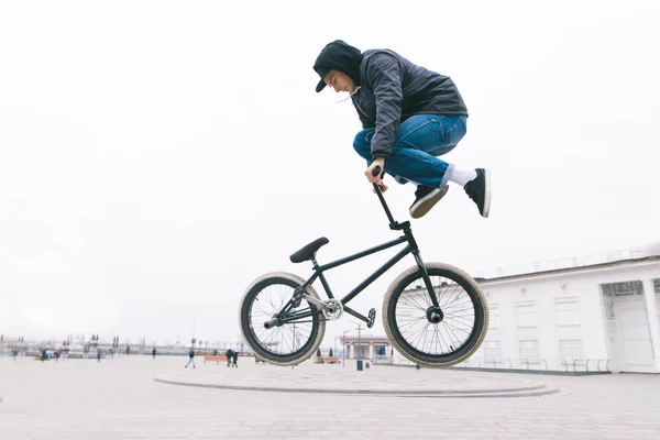 Bmx freestyle. BMX-cyklist gör komplexa trick på en cykel. Ung man gör spektakulära stunts mot bakgrund av stadens torg. — Stockfoto