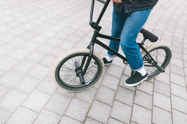 Een jonge chelovek zit op een Bmx fiets. BMX met benen close-up. BMX concept. Straatcultuur weg te zinken — Stockfoto