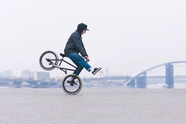 Young Bmx fiets renner rijdt op het voorwiel tegen de achtergrond van de minimalistische stadslandschap. BMX concept. — Stockfoto