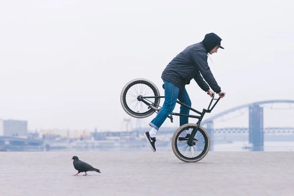 Un joven con ropa casual monta en una rueda delantera de bicicleta bmx. acrobacias en bmx —  Fotos de Stock