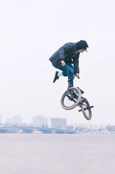 Mladý muž dělá triky na Bmx kole. BMX freestyle proti pozadí městské krajiny — Stock fotografie