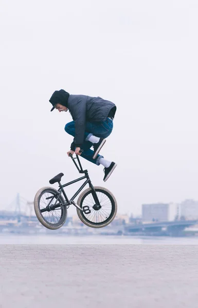 BMX freestyle. Egy fiatal férfi tesz egy légi mutatványokat egy Bmx kerékpár. A háttérben a városi táj — Stock Fotó