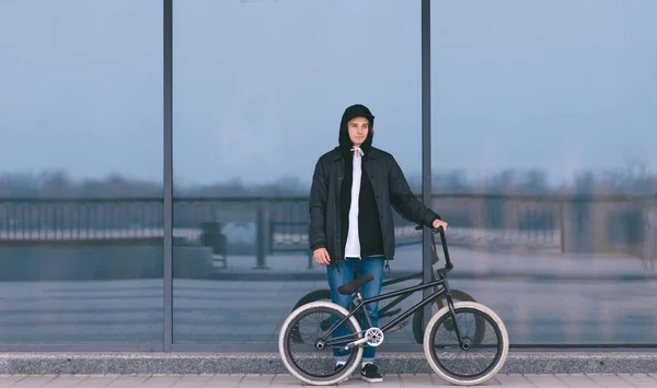 Sullo sfondo di una parete scura si erge un giovane con una bici BMX. Ritratto di ciclista BMX. Cultura di strada — Foto Stock