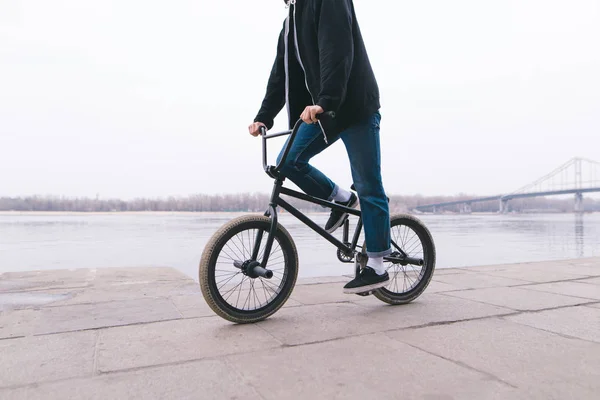 Een jonge man rijdt een Bmx fiets aan de waterkant in de buurt van de rivier. Lopen op Bmx. — Stockfoto