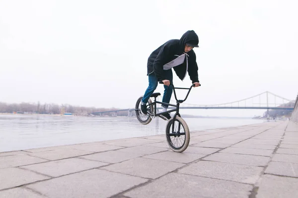 BMX freestyle. Un joven está haciendo trucos en una bicicleta BMX cerca del río — Foto de Stock