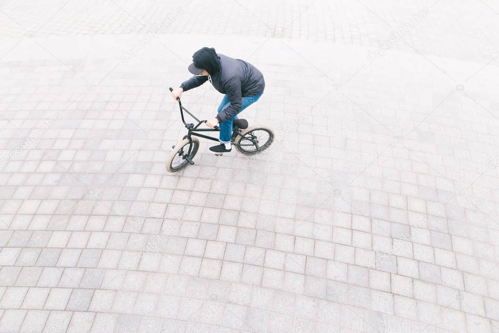A man rides a BMX bike on a pavement overhead. Minimalist photo of cyclist who rides on BMX in the square