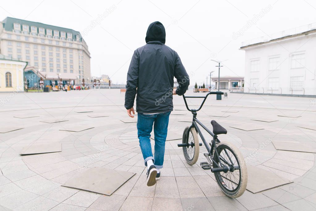 A spine of a young man walking around the city with a BMX bike. Walk with a bike. A cyclist travels along the street with a bike. BMX concept
