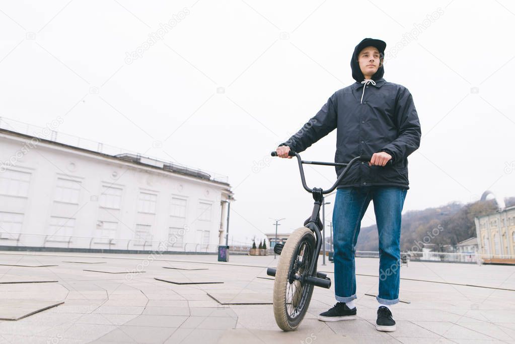 Portrait of a young man standing with a BMX bike against the city background. BMX rider stands with a bike. BMX concept