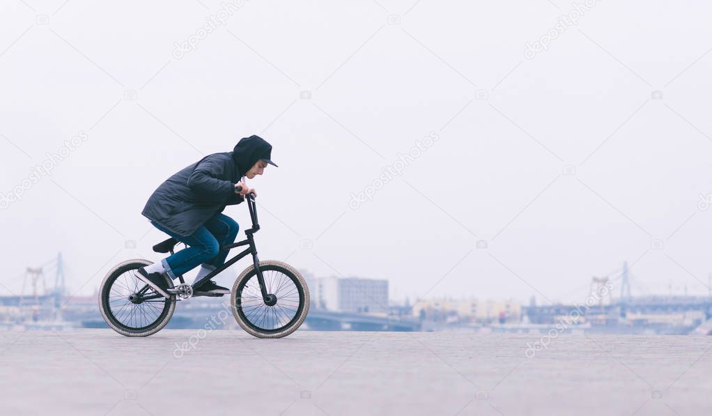 Street culture. Young BMX rider riding a bike on a minimalist city background. BMX cyclist is going to make a trick. BMX concept