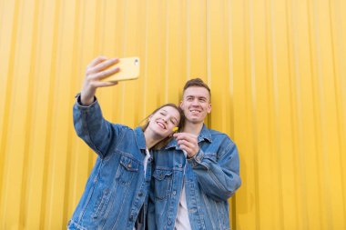 Mutlu çift sarı duvar bir arka plan üzerinde selfie yapıyor. Gülümseyen adam ve kız sarı bir arka plan üzerinde fotoğraflandı. Yenilikçi bir çift selfie yapar