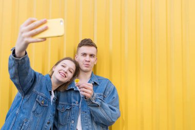 Şık çift denim ceket içinde selfie sarı bir arka plan üzerinde yapar. Duvardaki Selfies arka plan rengi.