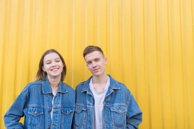 Güzel genç çift sarı bir arka plan üzerinde. Hipsters kot büküm bir çift sarı bir duvar arka plan üzerinde duruyor