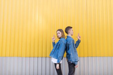 Genç güzel çift ayakta arkaya silah şeklinde elele. Bir çift sarı bir duvar arka plan üzerinde şık gençlerin