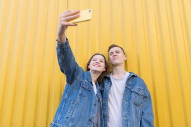 Mutlu, şık çift sarı bir duvar arka plan üzerinde bir smartphone cep telefonu ile fotoğraflandı. Adam ve kız selfie sarı duvar bir arka plan üzerinde yapmak