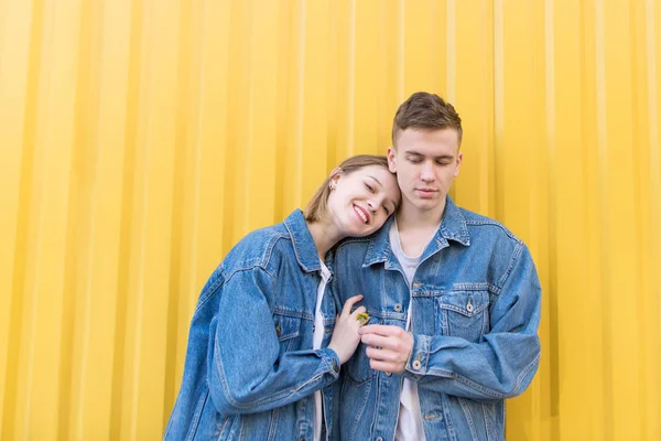 Casal feliz abraçando o fundo de espera. Retrato de um jovem casal em pé no fundo de uma parede amarela e sorrindo — Fotografia de Stock