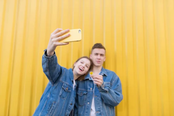 Frumos cuplu tânăr face selfie pe un fundal de perete galben. Concentrează-te pe smartphone. Selfie-uri pe smartphone — Fotografie, imagine de stoc