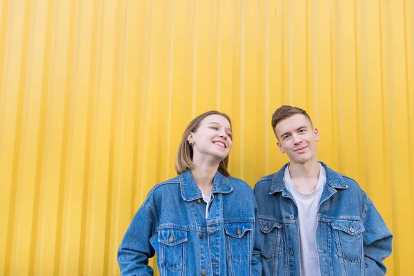 Retrato de um jovem casal contra um fundo de parede amarelo. Homem e menina elegantes estão em um fundo amarelo e sorrindo. Felizes jovens hipsters — Fotografia de Stock