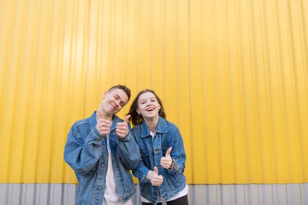 Um casal feliz mostra os dedos no fundo da parede amarela. Par elegante em pé sobre um fundo amarelo e regozijo. Espaço de cópia — Fotografia de Stock