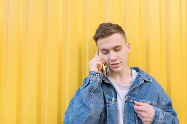 Портрет красивого молодого человека, разговаривающего по телефону на фоне желтой стены и улыбающегося. Стильный, счастливый хипстер, говорящий на смартфоне на ярком фоне — стоковое фото