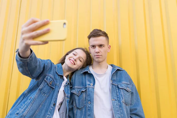 Красивая пара делает селфи на цветном фоне. Молодая пара фотографируется на смартфоне. Изолированный на желтом фоне — стоковое фото