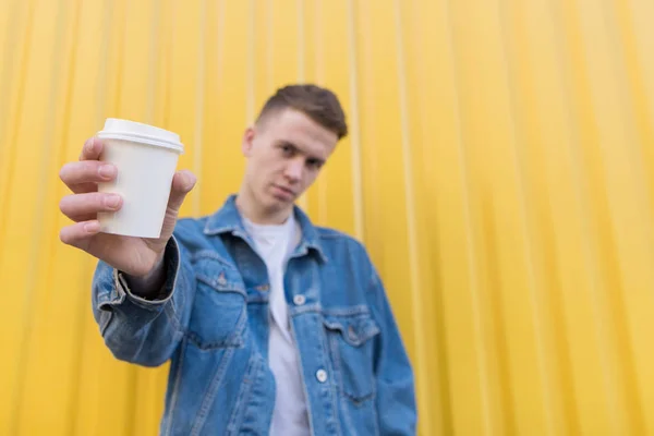 Um jovem elegante oferece café. Uma xícara de café nas mãos de um homem é enviada para a câmera. Xícara com café close-up. Espaço de cópia . — Fotografia de Stock