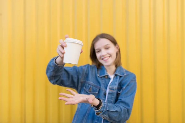 Чашка кофе в руках счастливой девушки на желтом фоне. Девушка держит в руках белую чашку. Кубок в фокусе — стоковое фото
