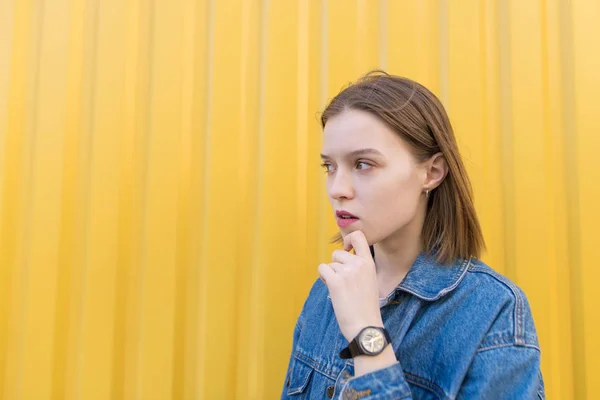 Zamyšlená dívka stojí na pozadí žluté zdi a vypadá na stranu — Stock fotografie