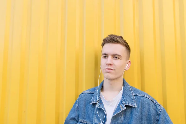 Portrait d'un jeune homme élégant écoutant de la musique sur le fond d'un mur jaune. Un jeune homme écoute de la musique sur un casque sur fond jaune — Photo