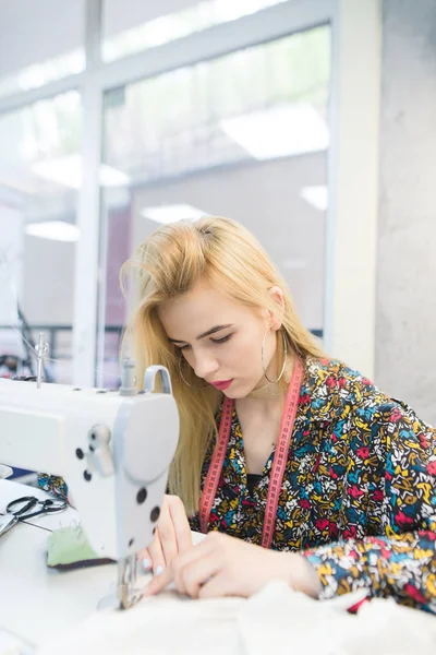 En ung sömmerska arbetar på en symaskin på arbetsplatsen. Vacker flicka fungerar på en symaskin. Sömmerska arbete på symaskinen. — Stockfoto