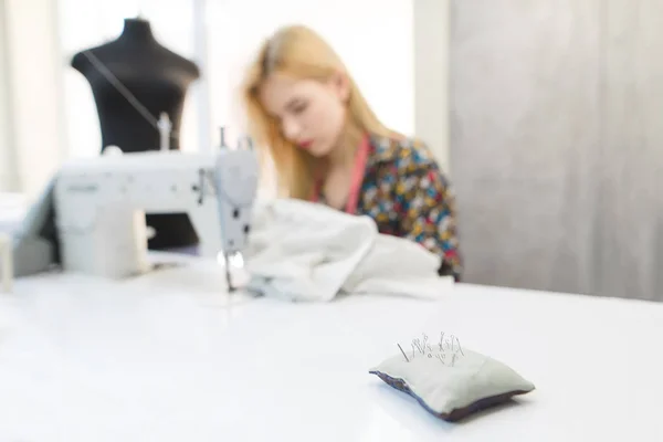 Agujas en una almohada en el fondo de costureras que trabajan en una máquina de coser y un maniquí. Lugar de trabajo para costureras. Concepto de costura. Trabajo de modista — Foto de Stock