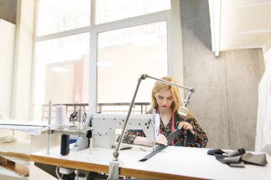 Portre sevimli bir genç terzi anda giysi tasarımı hafif bir salonda profesyonel bir dikiş makinesi üzerinde. Terzi kavramı. Parlak modern Studio giysi Tasarımcısı oluşturulması.