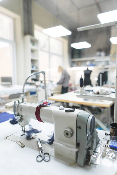 Work place for seamstresses. Professional sewing machine on the background of atelier studio. Workplace of tailor - sewing machine, rolls of thread, fabric, scissors. Sewing business concept.
