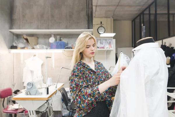 Красивая модельер девушка стоит в студии рядом с манекеном и фиксирует одежду на нем. Создание модной одежды. Концепция одежды дизайнера — стоковое фото