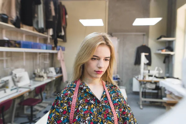 Retrato de un diseñador de ropa en el trabajo en el fondo de un estudio. Linda joven diseñadora de ropa elegante. Concepto de costura — Foto de Stock