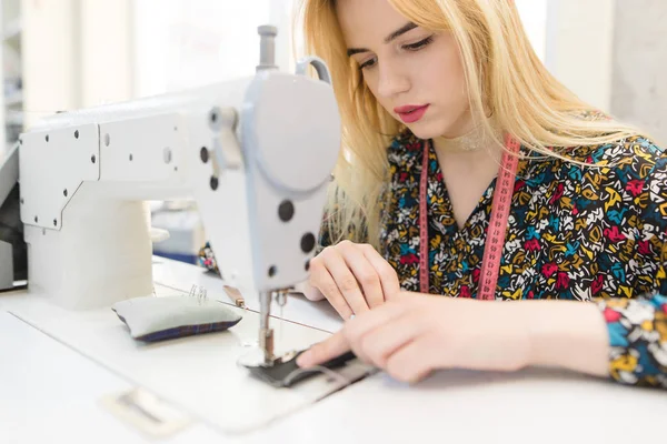 Portre portre sevimli bir genç terzi oturan ve bir dikiş makinesi dikiş. Profesyonel stüdyoda donatılmış terzi işleri. — Stok fotoğraf