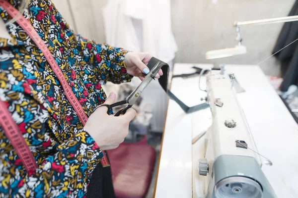 Švadlena ruce řez tkanina s nůžkami na pozadí šicí stroj a na pracovišti. Švadlena ve studiu na šití oblečení. Pracoviště na míru. — Stock fotografie