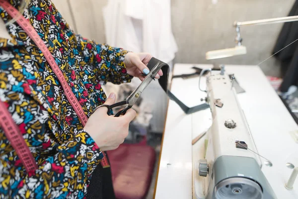 Švadlena ruce řez tkanina s nůžkami na pozadí šicí stroj a na pracovišti. Švadlena ve studiu na šití oblečení. Pracoviště na míru. — Stock fotografie