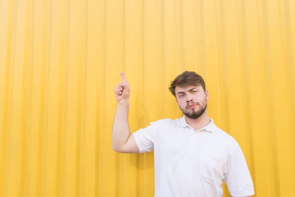 ハンサムな男は、黄色の背景の上に立つし、copyspace で手を示しています。白い t シャツを着た男は、copyspace の脇指を指示します。. — ストック写真