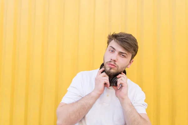 Retrato de um homem bonito com fones de ouvido no pescoço contra um fundo de parede amarelo. Estudante com fones de ouvido em um fundo amarelo — Fotografia de Stock