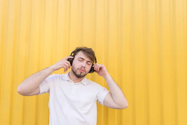 Красивый мужчина с закрытыми глазами слушает музыку на беспроводных наушниках на жёлтом фоне. Удовольствие от музыки . — стоковое фото