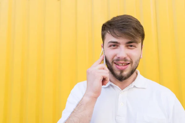 Retrato de un hombre feliz hablando por teléfono sobre el fondo de una pared amarilla y sonriendo. Un hombre sonriente hablando por teléfono sobre un fondo amarillo — Foto de Stock