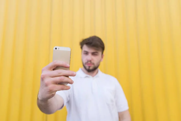 Hombre feliz sobre un fondo amarillo hace que el teléfono inteligente selfie en la mano. Concéntrate en el smartphone — Foto de Stock