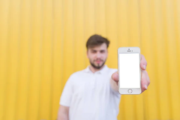 Der Mann steht auf gelbem Hintergrund und zeigt das Telefon mit weißem Bildschirm. Bildschirm für Kopierraum — Stockfoto