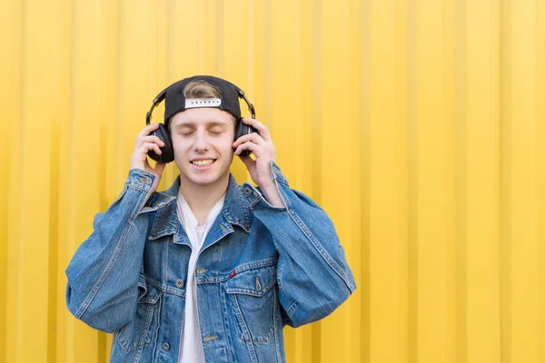 Happy Hipster escucha música en auriculares con los ojos cerrados en el fondo de la pared amarilla. Concepto musical . —  Fotos de Stock