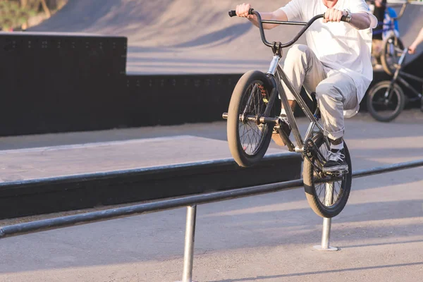 Un giovane uomo in abbigliamento leggero scivola sulla ringhiera sulla ruota posteriore di una bici BMX. acrobazie nello skate park sulla BMX. concept BMX — Foto Stock