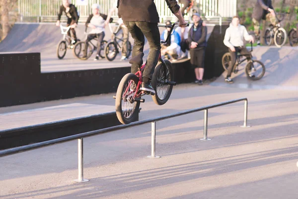 BMX cyclist makes tricks on rails in a skate park on the background of people with bikes. Jump to bmx . BMX tournament in a skatepark. BMX Concept. — Stock Photo, Image