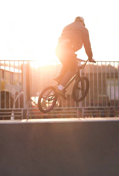 Bmx rider jumps on a bike in a skate park against the background of the sunset. A young man performs tricks on bmx in a skate park. Bmx concept — Stock Photo, Image